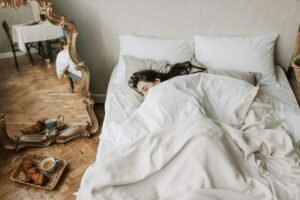 A woman peacefully sleeping in a cozy bed with croissants on the floor.